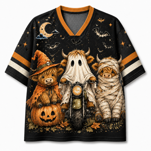 A black short-sleeve V-neck jersey-style shirt with orange and white sleeve stripes, featuring a large Halloween graphic print of three small Highland cows dressed as a witch, a ghost, and a mummy, with a pumpkin, motorcycle, bats, stars, and moon on a light gray background.