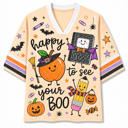 A light peach V-neck t-shirt with a colorful Halloween graphic print featuring a smiling pumpkin in a witch hat, a book with a face, a pencil character, bats, stars, and the text 'happy to see your BOO'.