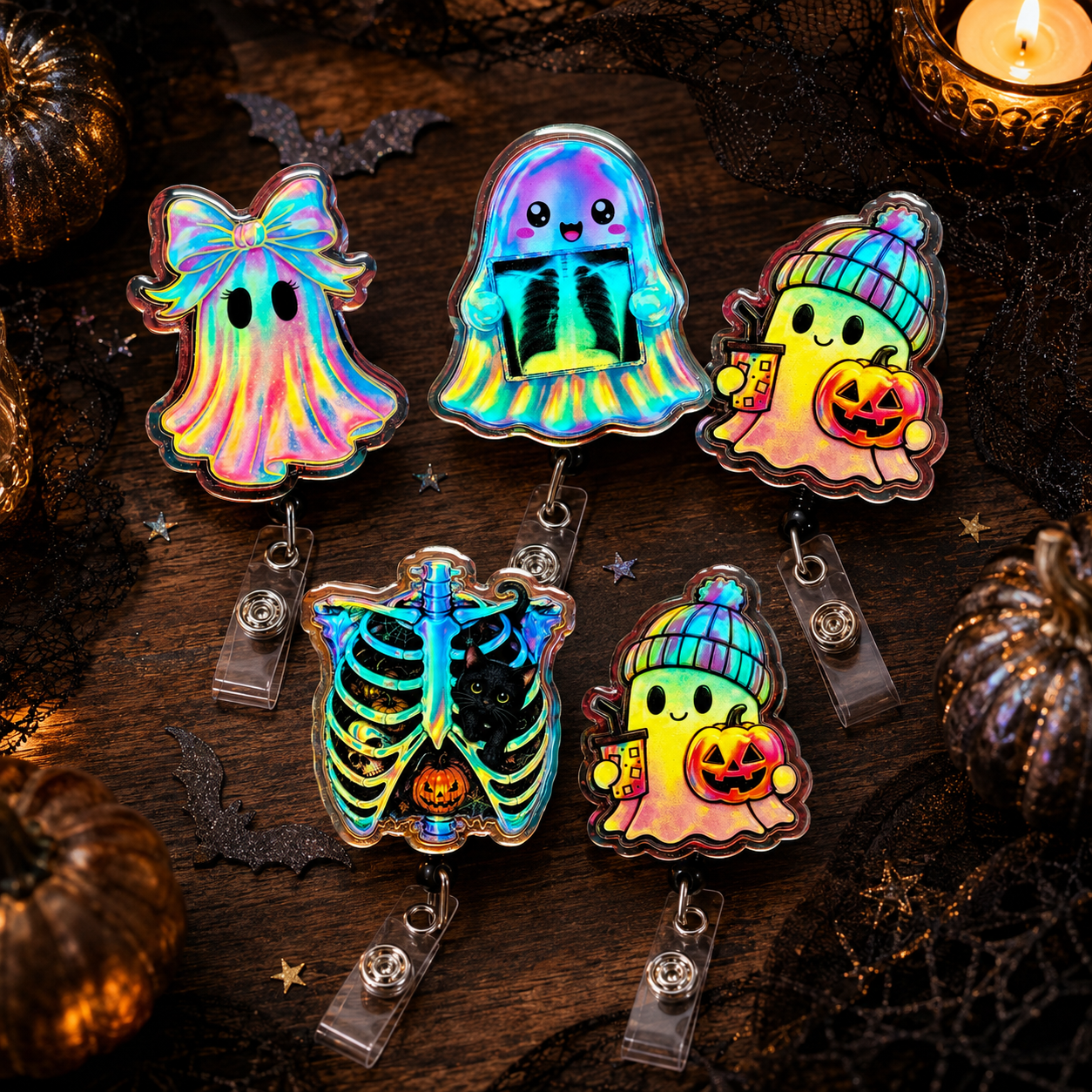 Five holographic Halloween-themed badge reels arranged on a dark wooden surface with spooky props. The designs include a ghost with a bow, a rainbow ghost, a ghost holding a pumpkin and beanie, a rib cage with a black heart, and a ghost in a striped beanie holding a pumpkin.