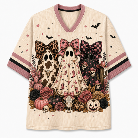 A cream-colored V-neck t-shirt with a detailed Halloween graphic featuring three cartoon ghosts in leopard, pink-and-black check, and cow-print outfits, surrounded by pumpkins, roses, skulls, and bats. The sleeves have pink and black stripes.