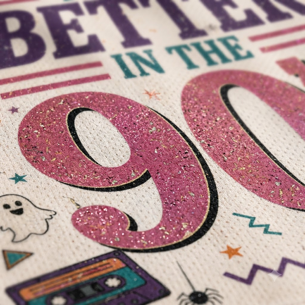 A close-up of a textured fabric print featuring a glittery pink '90' with retro Halloween graphics, including a cassette tape, spider, ghost, stars, and the text 'BETTER IN THE'.