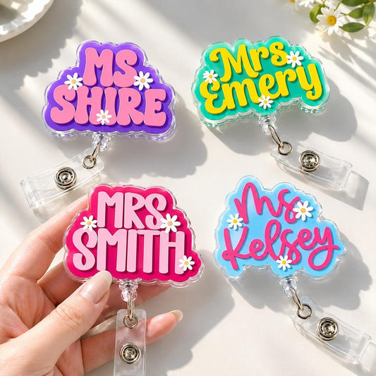 Four colorful name badge holders with names 'MS SHIRE', 'Mrs Emery', 'Mrs Smith', and 'Mrs Kelsey' on a light background.