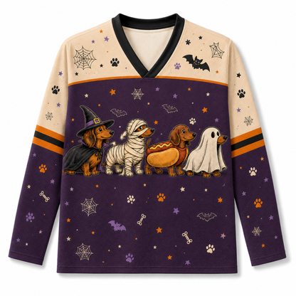A long-sleeve V-neck shirt with a Halloween dog-themed graphic print. The design features four dachshunds dressed as a witch, mummy, hot dog, and ghost on a dark purple background with spiderwebs, stars, and paw prints.