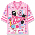 Front view of the pink ChaoticClub Preppy Back To School Teacher Pennant Flag Mesh Jersey, featuring a pink Counselor pennant, globe, notebooks, apple, and custom "Mrs. Smith" text.