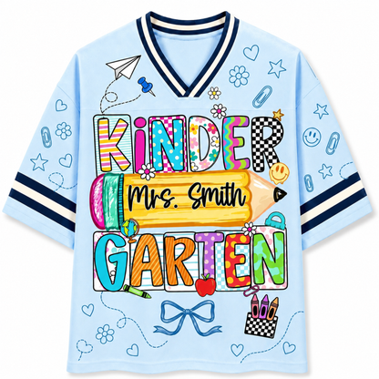 Front view of the light blue ChaoticClub Doodle Back to School Teacher Mesh Jersey, featuring colorful patchwork "KINDERGARTEN" text, a large yellow pencil graphic with customizable "Mrs. Smith" name, and small school doodles.