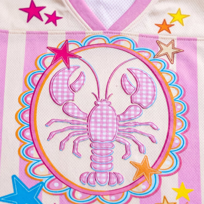 Colorful embroidered design of a lobster on fabric with star accents.