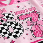 A close-up of a pink mesh garment, likely a sports jersey or top, featuring a graphic design with the text 'NOW I AM' and stylized numbers 0 and 1. The number 1 has a pink leopard print pattern with a pink bow, while the number 0 has a black and white checkerboard pattern.