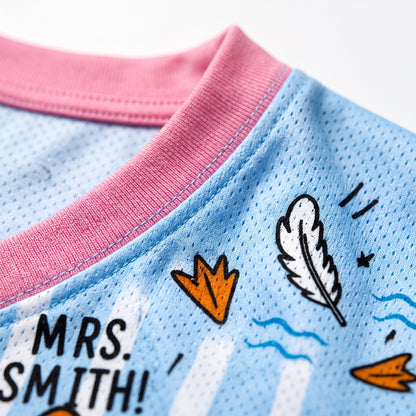 Close-up of a sports jersey with 'MRS. SMITH!' text and feather design on a blue and pink background.