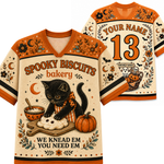 A Halloween-themed v-neck t-shirt shown from both front and back. The shirt features a cream base with orange shoulder panels and collar, decorated with illustrations of a black cat kneading a biscuit, pumpkins, bats, and stars.