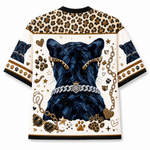 A short-sleeve crewneck shirt with a cream base, featuring a large graphic of a black cat wearing a silver chain collar with a heart emblem. The shirt is decorated with leopard print patterns on the shoulders, sleeves, and borders, along with paw prints, hearts, stars, and sunglasses.