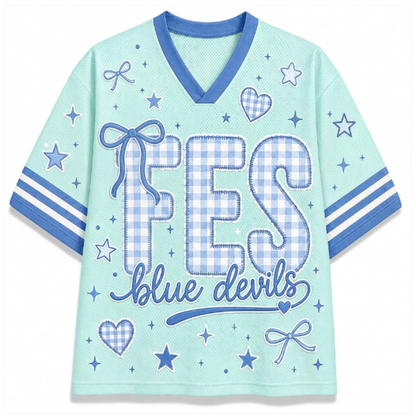 A light mint green short-sleeve V-neck t-shirt with blue trim, featuring a 'FES blue devils' graphic on the front with gingham patterned letters and blue star, heart, and bow motifs.