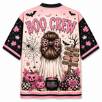 A short-sleeve t-shirt with a pink and black Halloween-themed graphic print. The back of the shirt features the text 'BOO CREW' in dripping pink letters above an illustration of a girl with a leopard-print bow, surrounded by pumpkins, a cauldron, bats, and a spiderweb.