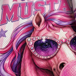A close-up of a pink and purple graphic print featuring a stylized horse face with oversized rhinestone sunglasses, a star on its forehead, and partial text reading 'MUSTA' at the top. A folded section of matching patterned fabric is visible on the right edge.