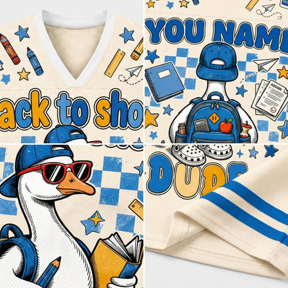 A close-up collage of a cream-colored athletic jersey or sweatshirt fabric with blue and yellow printed graphics. The design includes a V-neck, mesh texture, blue stripes, a cartoon duck wearing a blue cap and sunglasses with a backpack, stars, pencils, books, and text such as 'YOU NAME' and 'DUDS'.