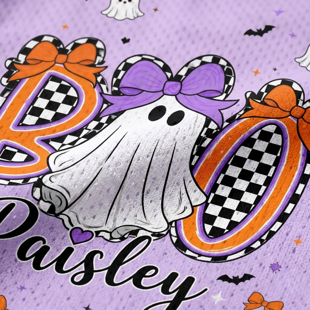 Close-up of a purple fabric featuring a Halloween-themed personalized design with the name 'Paisley' in black script, a white ghost with a purple bow, and large orange-and-black checkered letters spelling 'BOO'.