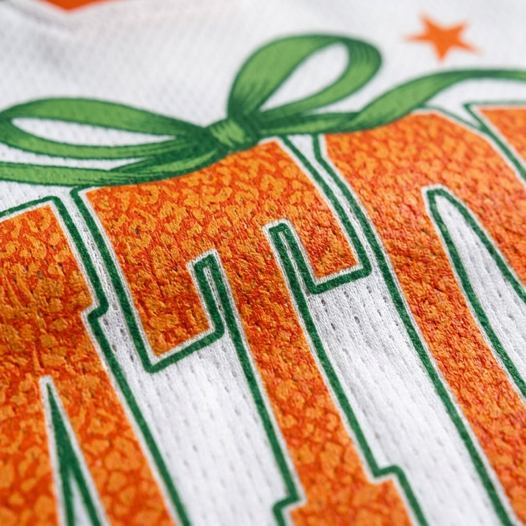 Close-up of a white athletic jersey with a large orange and green graphic, showing part of the word 'ATLANTA' and a green ribbon motif.