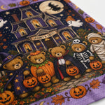 A close-up of a Halloween-themed fabric featuring teddy bears dressed as a witch, pumpkin, skeleton, and mummy in front of a haunted house, with pumpkins, ghosts, and a moon on a purple background.