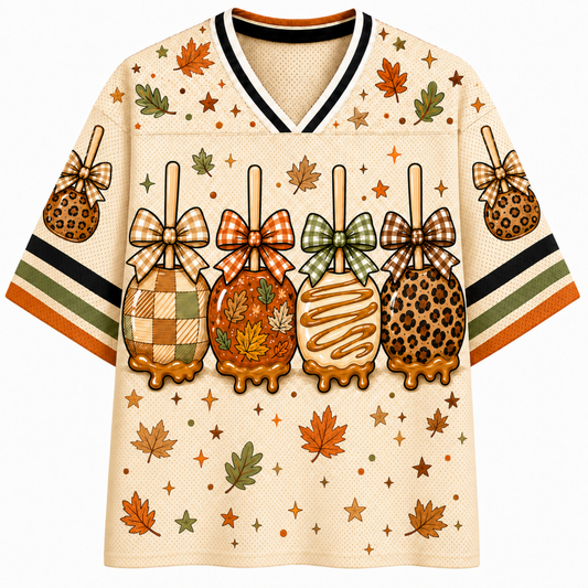 Front view of the cream varsity jersey displaying four caramel-dipped apples styled with plaid, maple leaf, and leopard patterns with coquette ribbon bows.
