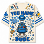 A cream-colored t-shirt with a large blue and yellow graphic print on the back. The design features a cartoon duck wearing a blue baseball cap and backpack, surrounded by school-themed doodles like stars, pencils, and a paint palette.
