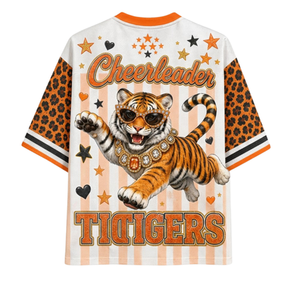 A short-sleeve graphic T-shirt shown from the back, featuring a white base with orange and peach vertical stripes, orange leopard-print sleeves, and a large tiger illustration wearing sunglasses with the words 'Cheerleader' and 'TIGERS'.