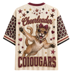 A cream-colored short-sleeve graphic t-shirt featuring a cougar mascot wearing sunglasses and a bow, with the word 'Cheerleader' and the word 'COUGARS' printed in maroon. The sleeves have a leopard print pattern with maroon and black stripes at the cuffs.