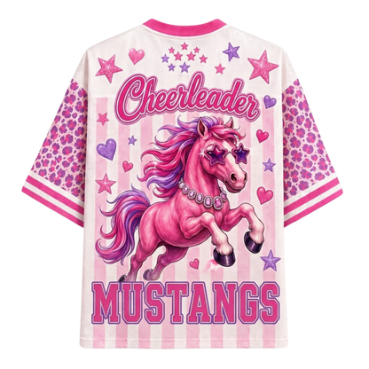 A women's short-sleeve graphic t-shirt featuring a pink and purple cheetah-patterned design. The back of the shirt displays a large illustration of a pink horse with purple accents, surrounded by pink and purple stars and hearts, with the text 'Cheerleader MUSTANGS' in pink.
