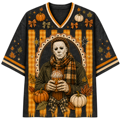 A black short-sleeve V-neck t-shirt featuring a detailed Halloween graphic of Michael Myers in a plaid sweater and scarf, holding a drink, surrounded by pumpkins, autumn leaves, and plaid bow motifs in orange, beige, and brown.