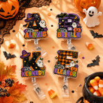 Four Halloween-themed acrylic name badges with clear plastic clip-on backs, decorated with letters A, B, K, and F, ghosts, pumpkins, bats, and autumn leaves on an orange fabric background with seasonal props.