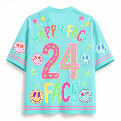 A light blue short-sleeve t-shirt with a colorful retro graphic on the back. The design features the text 'HAPPY FACE 24 FACE' in vibrant neon colors, decorated with smiley faces, stars, and circular patterns.