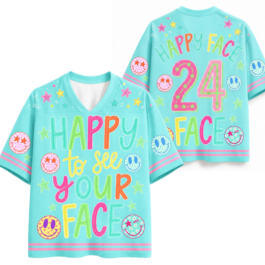 A light blue V-neck t-shirt with colorful retro-style graphics, shown in both front and back views. The front features the text 'HAPPY to see YOUR FACE' in multicolor bubble letters, decorated with smiley faces, stars, and the number '24' on the back.