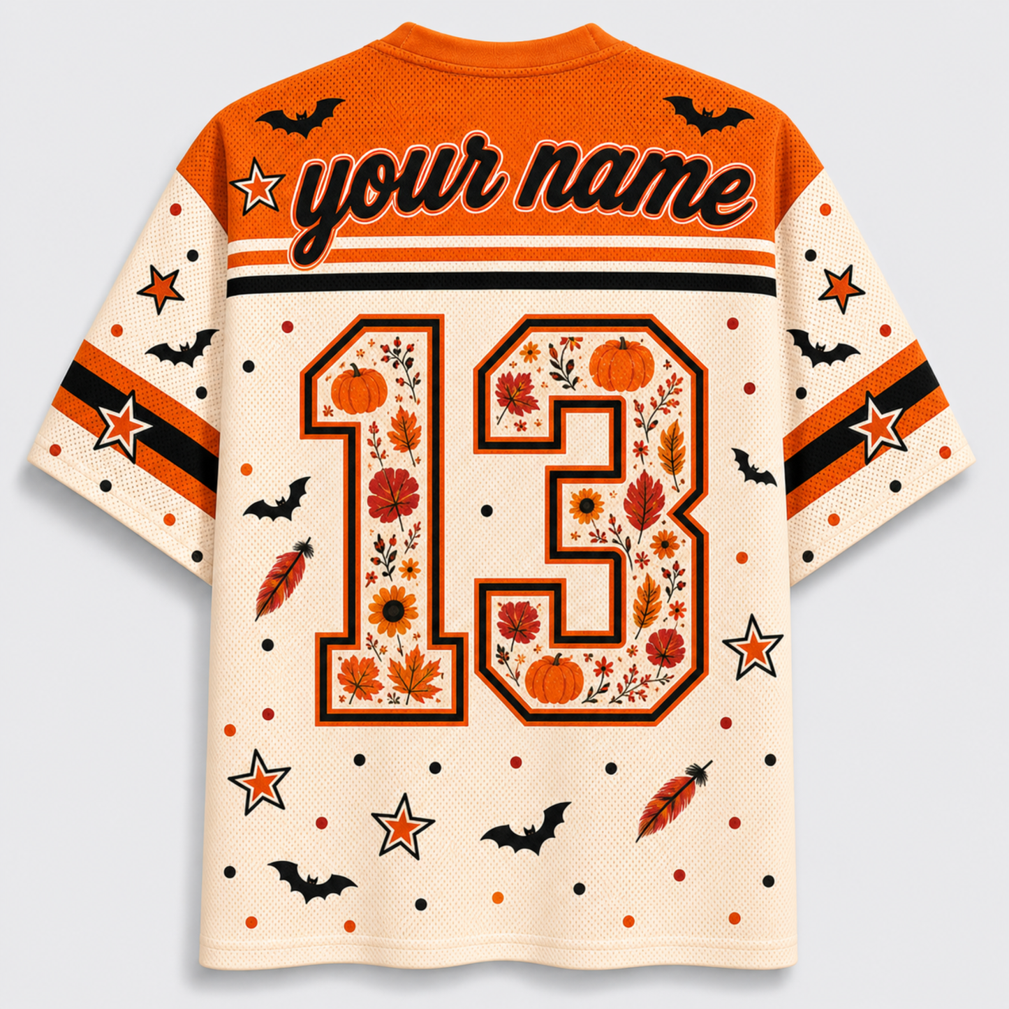 A short-sleeve mesh jersey-style shirt shown from the back on a light gray background. The shirt is cream with orange and black graphics, including the text 'your name', a large number 13 filled with autumn leaves and pumpkins, stars, bats, and feather motifs.