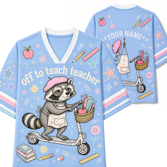 A light blue graphic t-shirt shown from both the front and back. The front features a cartoon raccoon wearing glasses and a pink beret, riding a scooter with books and a pencil basket.