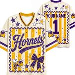 Customizable cream-colored jersey shirt mockup showing both front and back views. Features purple and yellow varsity-style graphics, including 'Horns' script, stars, bumblebees, a large bow motif, and placeholder text 'YOUR NAME' and number '1'.
