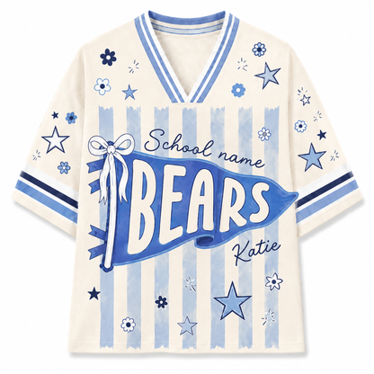 A cream-colored short-sleeve V-neck t-shirt with a blue and light blue sports-themed graphic. The design features a large blue banner reading 'BEARS' with 'School name' and 'Katie' written above and below, alongside blue stars, flowers, and vertical stripes.
