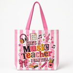 A pink and white striped tote bag featuring a colorful graphic that reads 'SHE'S A Music Teacher I CAN TELL' with school and music-themed illustrations including headphones, stars, a bow, books, and a pencil cup, shown on a clean white background.