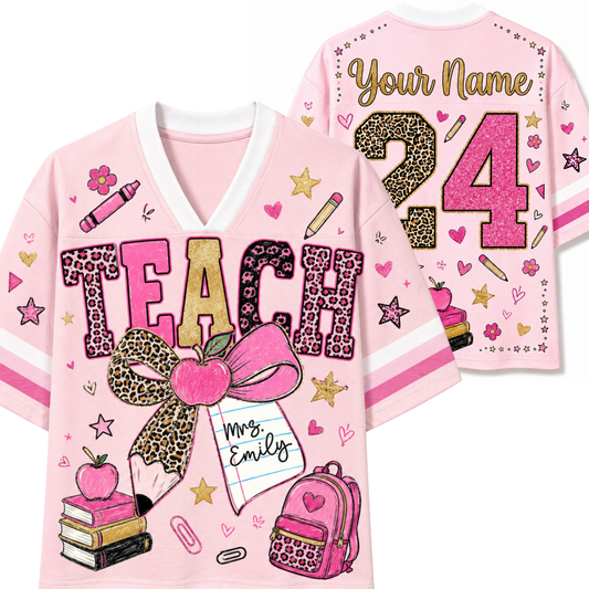 A pink short-sleeve V-neck jersey-style shirt shown from both front and back, decorated with school-themed graphics including the word TEACH, a large pink bow, an apple, books, a backpack, stars, hearts, and customizable text reading Your Name and 24.