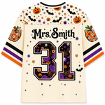 A cream-colored short-sleeve jersey with Halloween-themed graphics, including pumpkins, bats, stars, and purple swirls. The back of the jersey features the text 'Mrs.