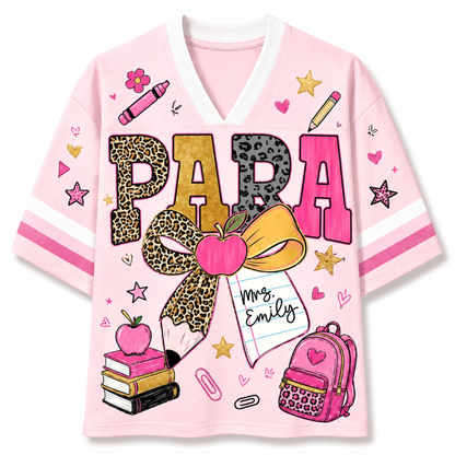 A light pink V-neck t-shirt with a colorful school-themed graphic on the front. The graphic features the word 'PAPA' in leopard-print and pink letters, a large leopard-print bow, a pink apple, a notebook that says 'Mrs.