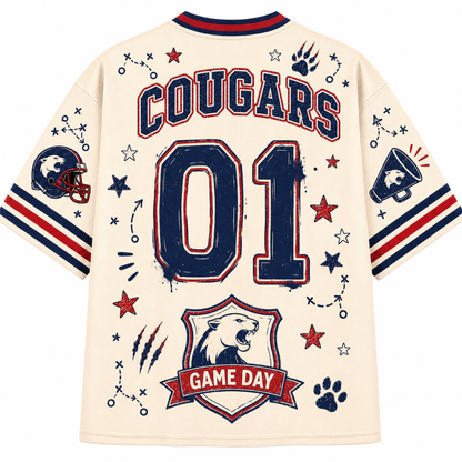 Back view of a cream-colored sports jersey featuring 'COUGARS' and '01' in navy and red, decorated with football-themed graphics including a helmet, paw prints, stars, and a 'GAME DAY' banner.