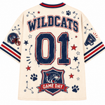 Back view of a cream-colored short-sleeve jersey with 'WILDCATS' and '01' printed in navy blue with red outlines, decorated with stars, paw prints, a football helmet patch, and a 'GAME DAY' shield on the lower back.