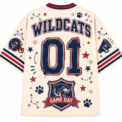 Back view of a cream-colored short-sleeve jersey with 'WILDCATS' and '01' printed in navy blue with red outlines, decorated with stars, paw prints, a football helmet patch, and a 'GAME DAY' shield on the lower back.