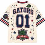 Back view of a cream-colored Florida Gators football jersey with 'GATORS' and '01' printed in navy and red, decorated with team-themed graphics including an alligator logo, stars, and a Game Day crest.