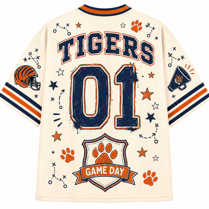 A cream-colored short-sleeve sports jersey shown from the back, featuring 'TIGERS' and '01' in navy blue with orange trim, along with orange paw prints, stars, a football helmet, a megaphone, and a 'GAME DAY' crest.