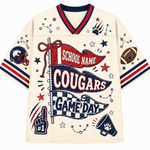 A cream-colored short-sleeve football jersey with red and navy blue trim, featuring a large 'COUGARS GAME DAY' graphic on the front with stars, paw prints, and sports-themed illustrations.