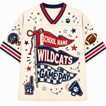 A cream-colored athletic jersey with navy and red trim, featuring a football-themed graphic design with 'SCHOOL NAME WILDCATS GAME DAY' banners, stars, paw prints, a football, and a helmet.