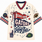 An off-white short-sleeve V-neck jersey-style shirt with red and navy trim, decorated with Florida Gators-themed graphics including a large 'GATORS' banner, 'SCHOOL NAME' flag, stars, paw print, football, eye patch, and pom key.