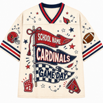 A cream-colored football jersey with navy and red trim, featuring a 'School Name Cardinals Game Day' banner graphic on the front, along with football-themed illustrations like a helmet, football, megaphone, and stars.