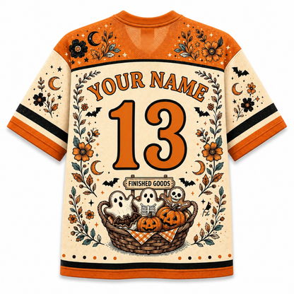 A custom Halloween-themed sports jersey shown from the back, featuring orange and cream colors with a floral, bat, ghost, and pumpkin graphic design. The back includes placeholder text 'YOUR NAME' and the number '13' with 'FINISHED GOODS' below it.