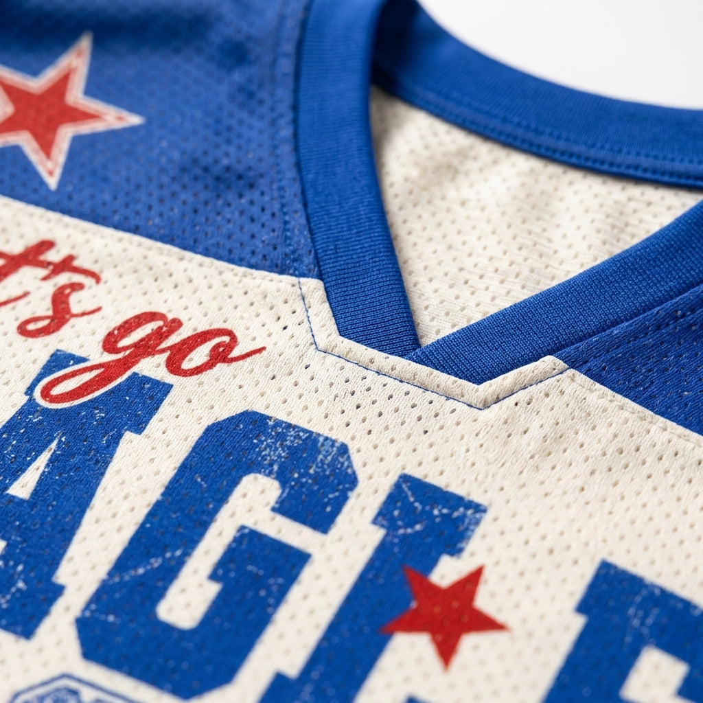 Close-up of a vintage-style athletic jersey showing a cream-colored mesh body, royal blue ribbed collar and lettering, and red star graphics.