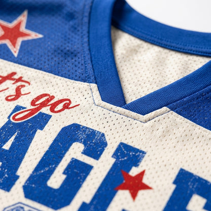 Close-up of a vintage-style athletic jersey showing a cream-colored mesh body, royal blue ribbed collar and lettering, and red star graphics.